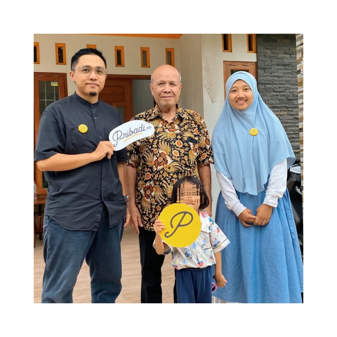 Achan dan Nisa berdiri bersama Abah Rama di depan rumah, memegang papan logo pribadi.